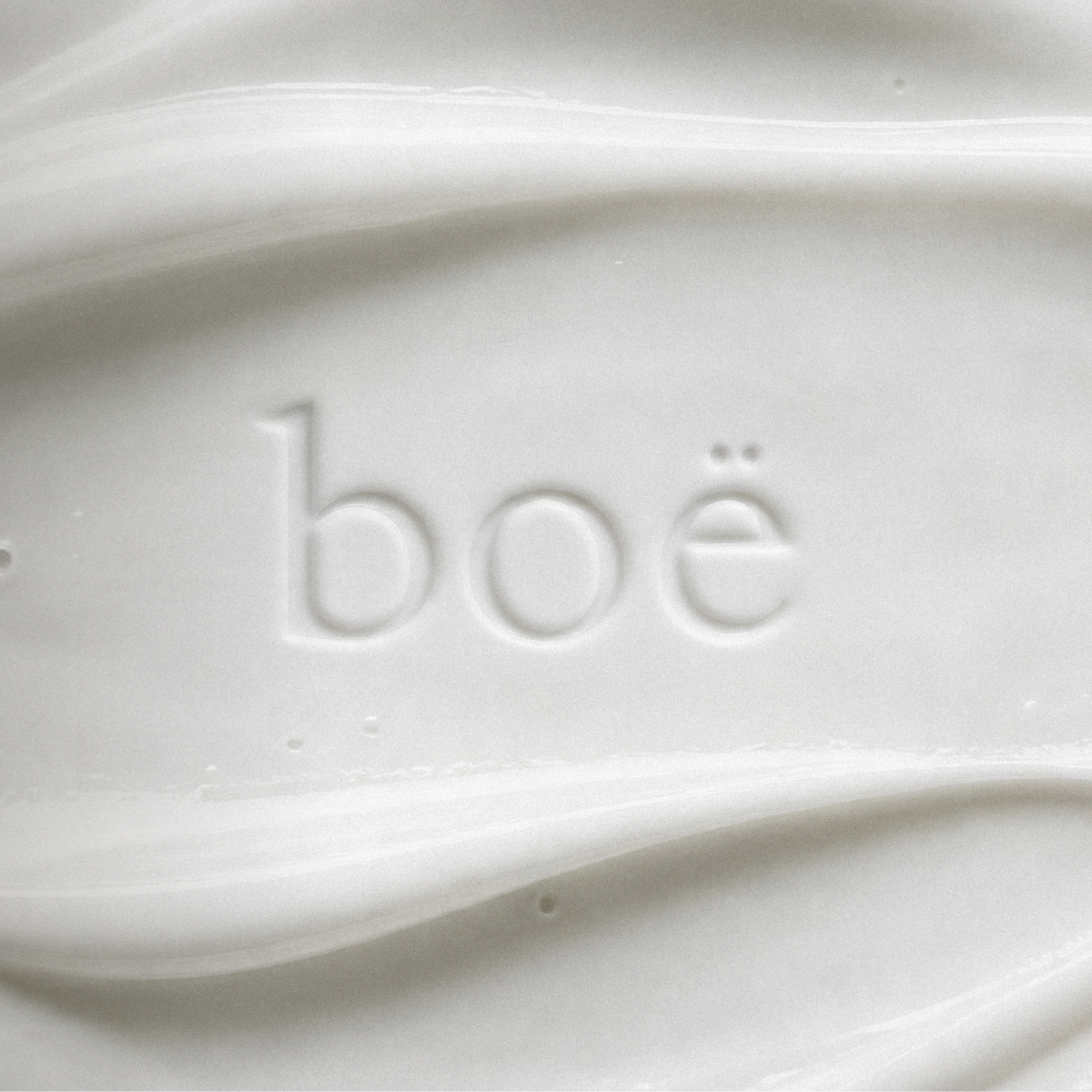 Close-up of a white skincare cream or tanning lotion with the brand name 'boe' embossed in the center. The image features elegant, soft draping textures and light text at the bottom reading 'skincare that tans.